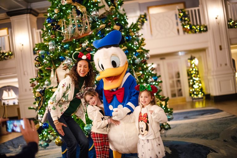 a group of people posing for a picture with a Donald Duck in front of a Christmas Tree