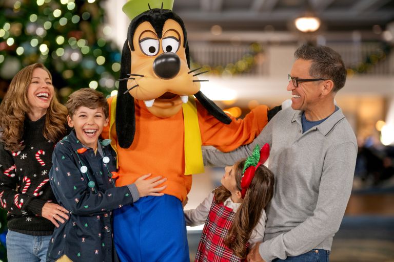 a man and two children hugging Goofy in front of a Christmas tree
